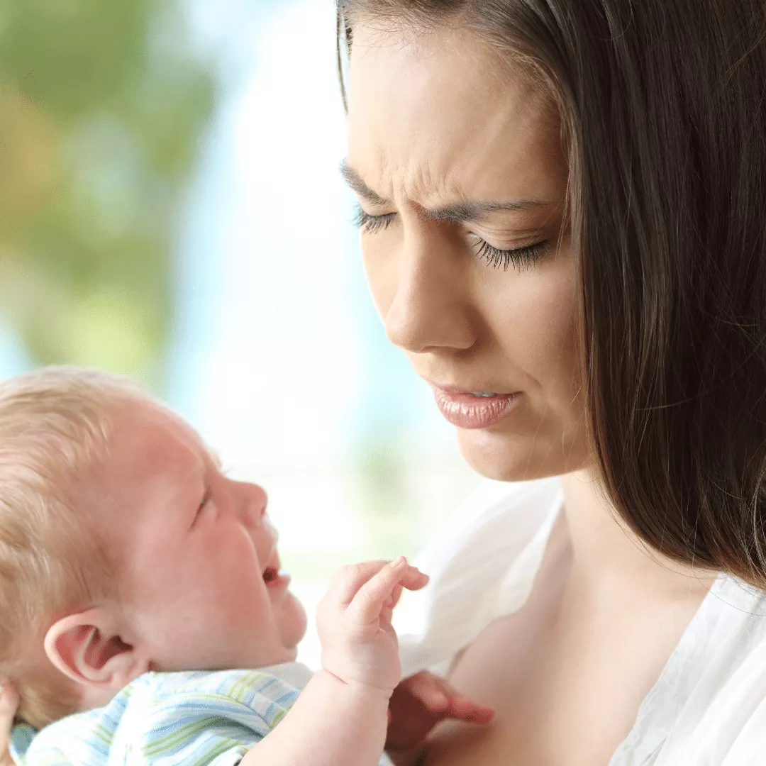 Schmerzende Brustwarzen beim Stillen: Frau hält Baby mit schmerzverzerrtem Gesicht